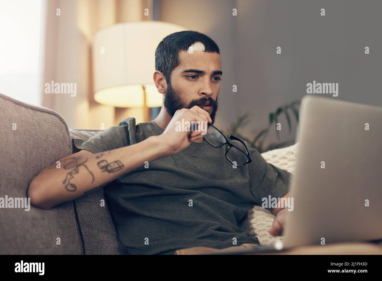 Bleiben Sie in Verbindung, bleiben Sie auf dem Laufenden über die Geschehnisse in der Welt. Aufnahme eines jungen Mannes, der zu Hause einen Laptop auf dem Sofa benutzt. Stockfoto