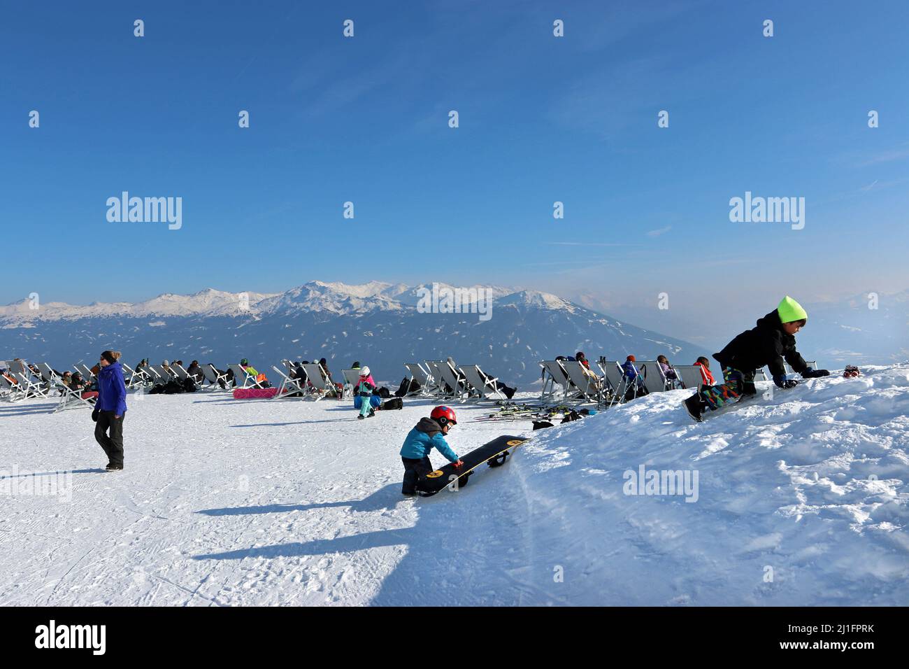 Kinder spielen im Schnee auf der Seegrube, nahe dem Gipfel des Hafelekar, in der Nordkette oberhalb von Innsbruck. Liegestühle von Cloud 9 Bar hinter Stockfoto