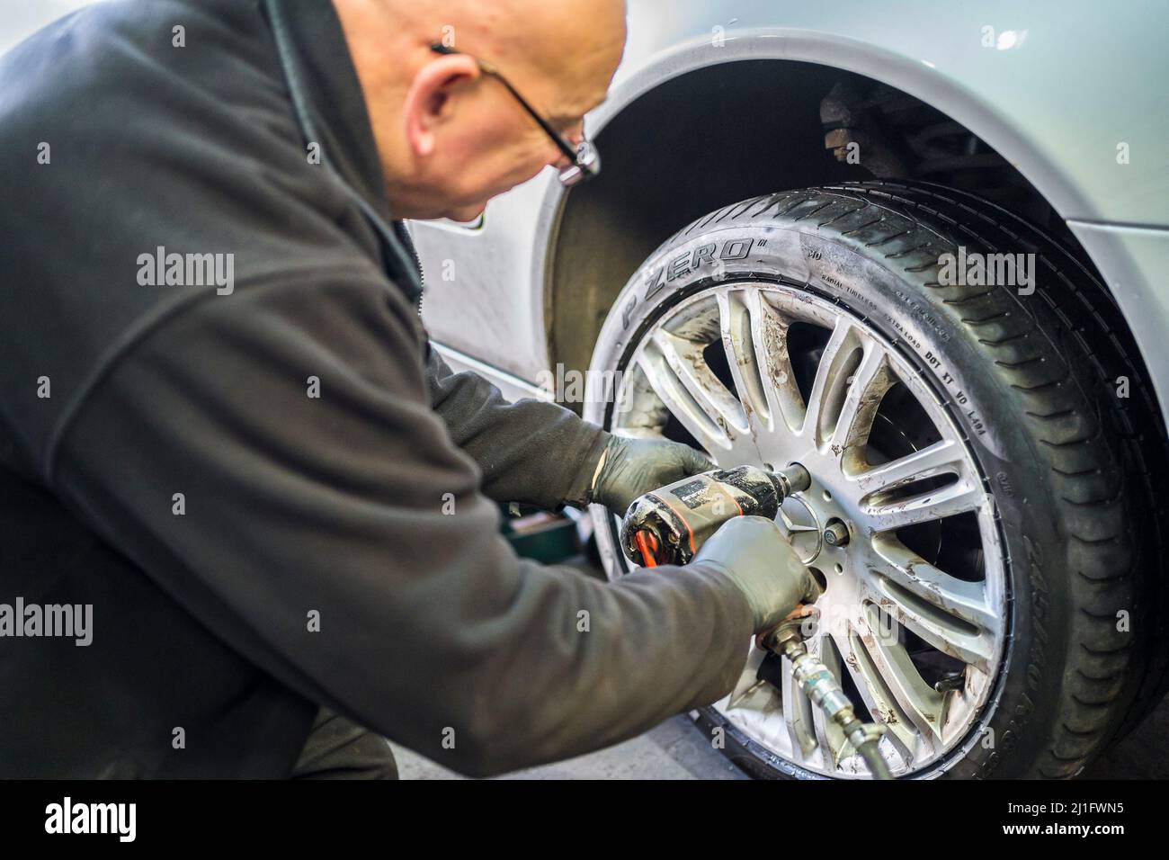 Reifenwerkstatt. Isolierter Mechaniker, der ein Leichtmetallrad an der Vorderachse eines Autos mit professioneller Luftaufprallschraubenpistole montiert. Stockfoto