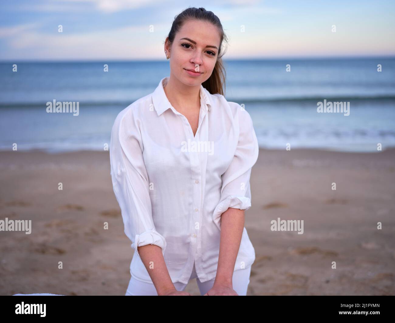 Eine junge, weiß gekleidete Chiromassage-Therapeutin, die an einem Strand in Valencia mit dem Meer im Hintergrund steht. Stockfoto