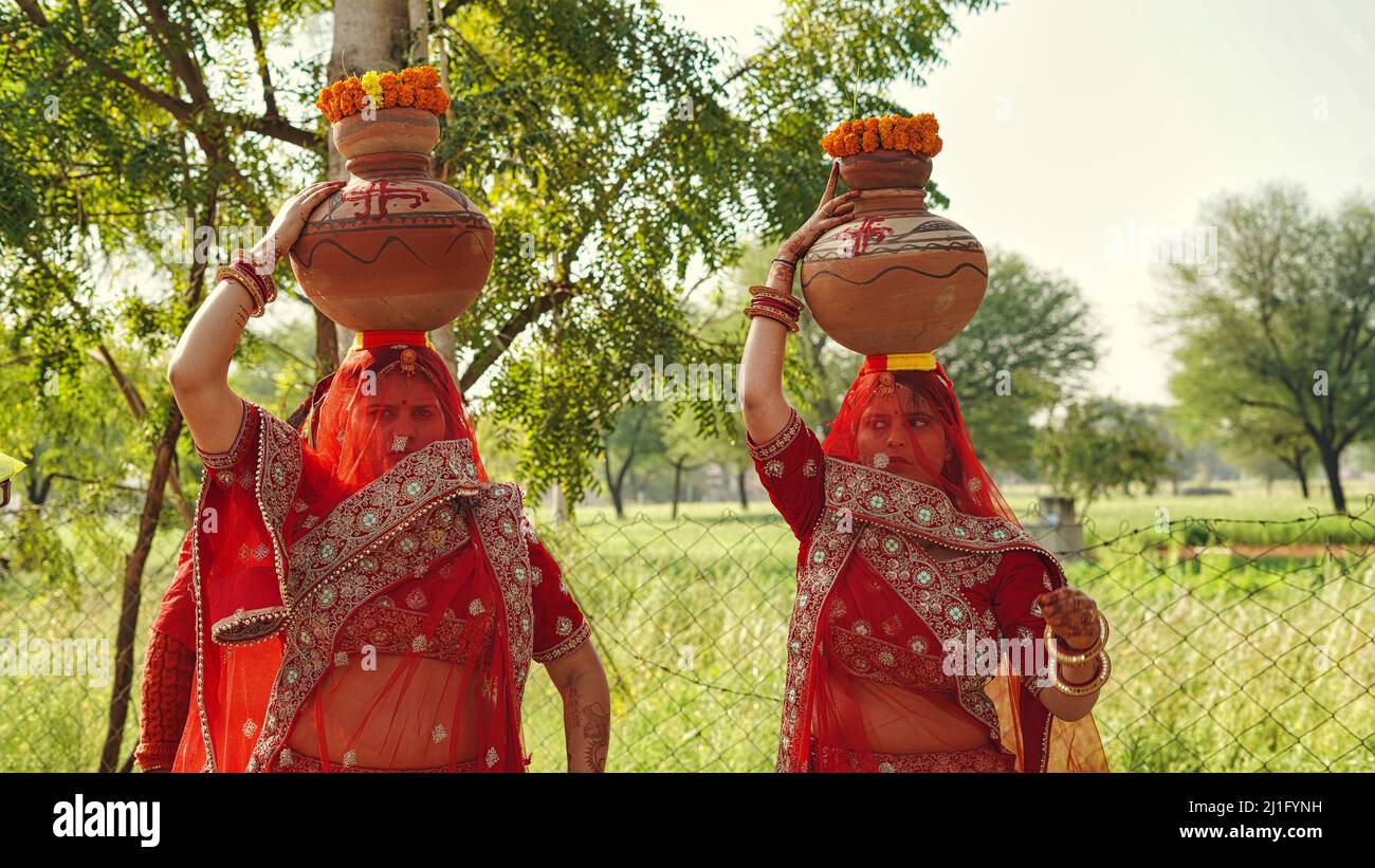 23 März 2022 Reengus, Rajasthan, Indien. Nicht identifizierte indische Neubraut in farbenfrohen traditionellen Kleidern trägt Wasser in Tontöpfen Stockfoto