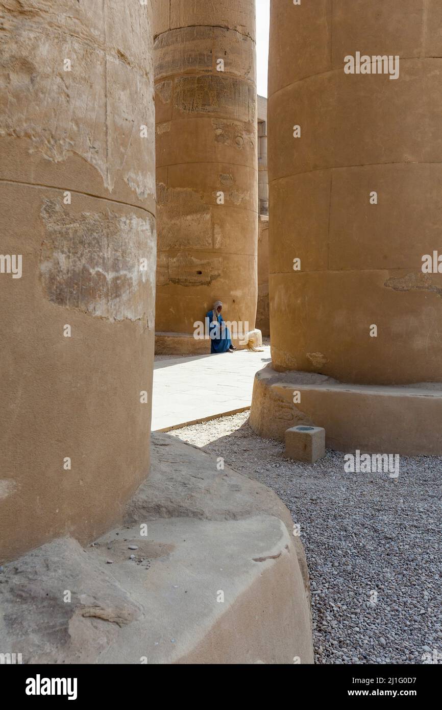 Örtlicher Arbeiter, der zwischen den Säulen der Prozessionskolonnade von Amenhotep III, Tempel von Luxor, sitzt Stockfoto