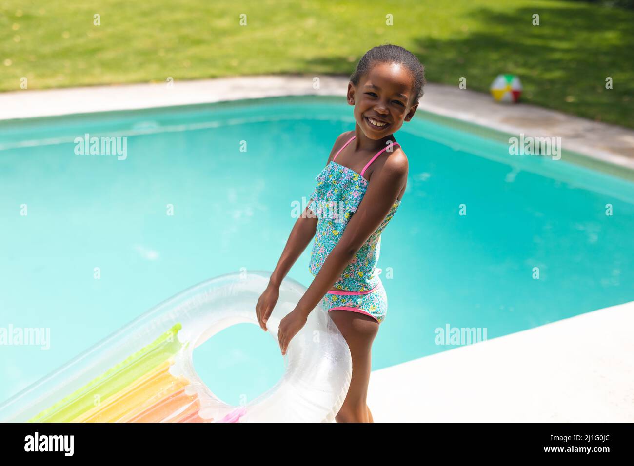 Porträt eines glücklichen afroamerikanischen Mädchens mit aufblasbarem Ring, das an einem sonnigen Tag am Pool steht Stockfoto