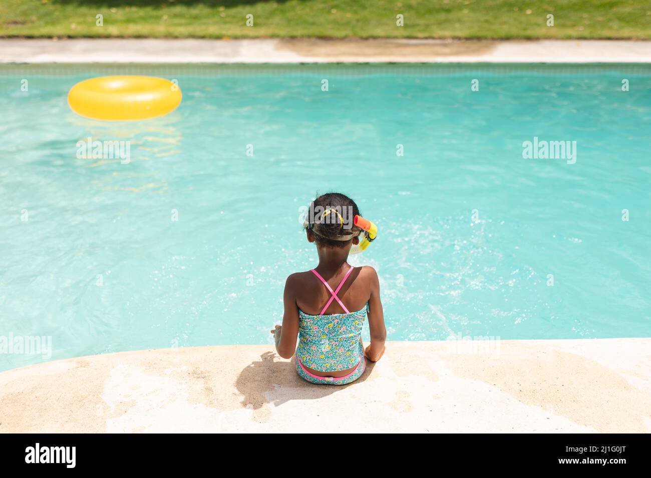 Rückansicht eines afroamerikanischen Mädchens mit Schnorchel, das an sonnigen Tagen am Pool sitzt Stockfoto