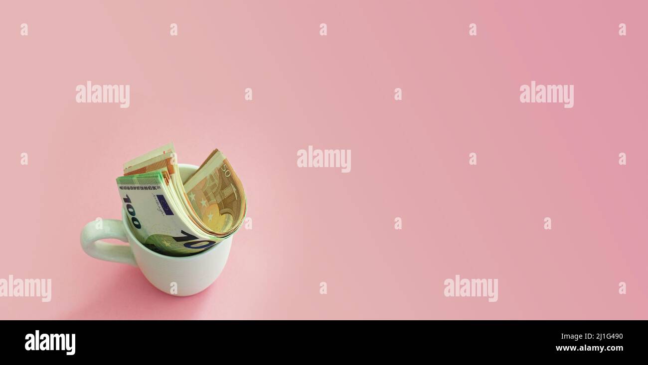 Euro-Banknoten in einer Kaffeetasse auf einem rosa Hintergrund. Geldkonzept. Unternehmen, Finanzen, Austausch Stockfoto Euro-Banknoten in einer Kaffeetasse auf einem rosa Hintergrund. Geldkonzept. Unternehmen, Finanzen, Austausch Stockfoto