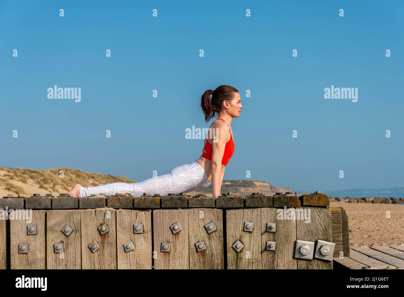 Sportliche junge Frau Stretching in Urdhva mukha shvanasana Übung, nach oben schauende Hund Pose. Schlanke Mädchen üben Yoga im Freien blauen Himmel. Stockfoto