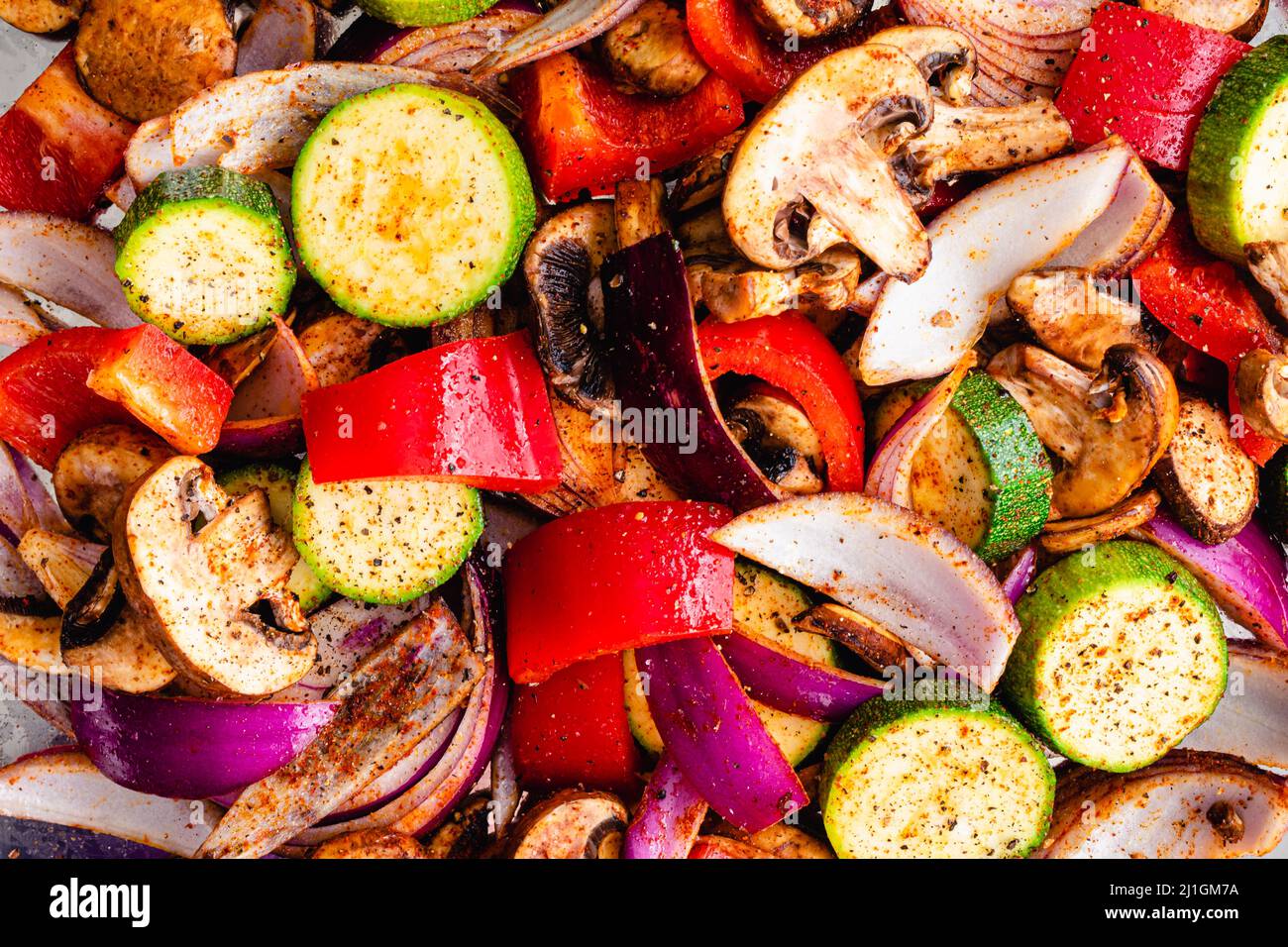Nahaufnahme Ansicht von rohem Gemüse gewürzt mit Olivenöl und Gewürzen: Ansicht von oben aufgeschnittenem und gewürztem Gemüse auf einer Blechpfanne Stockfoto