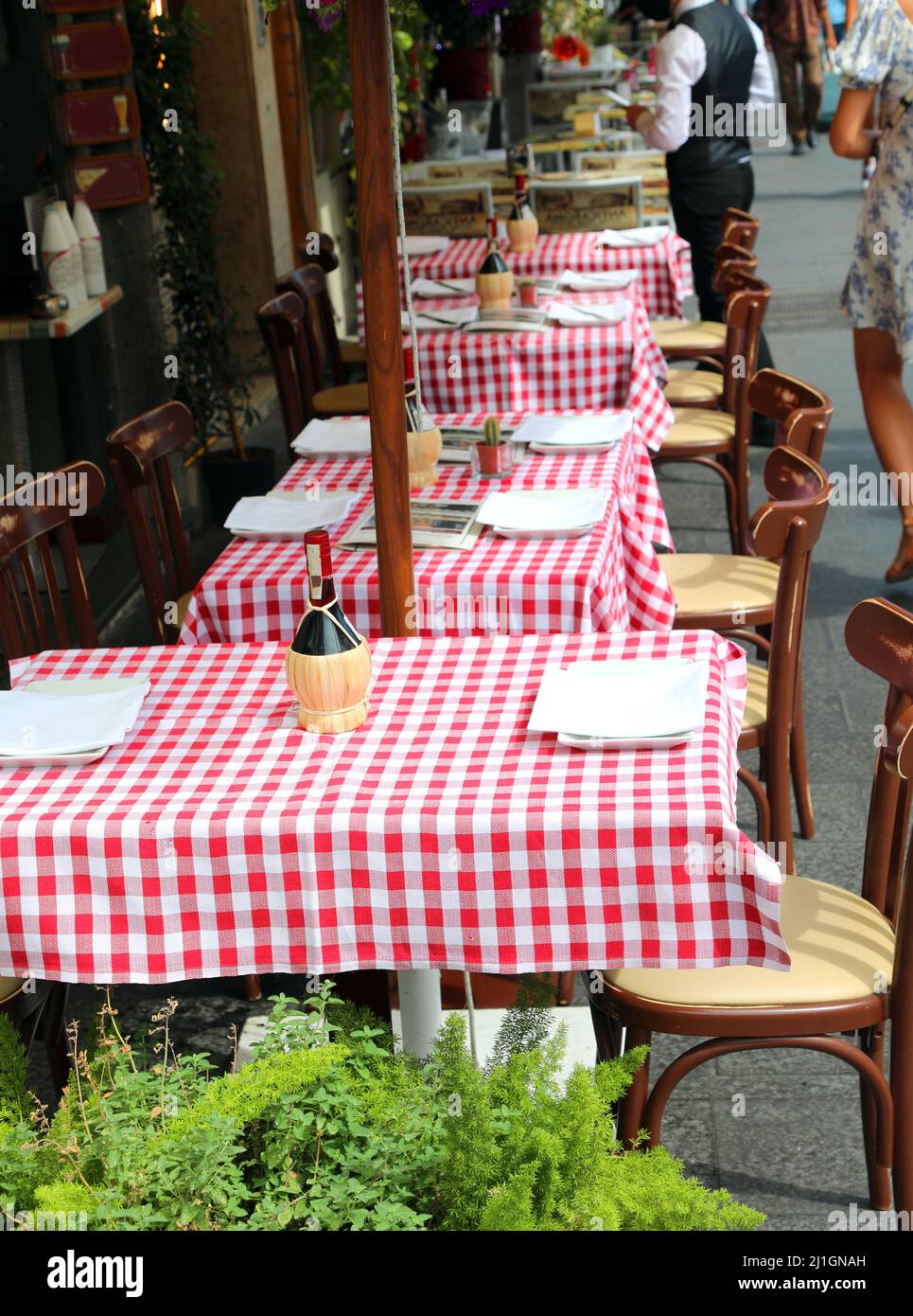 Tische und Stühle mit rot-weiß karierten Tischdecken in einem Alfresco-Restaurant ohne Kunden Stockfotografie
