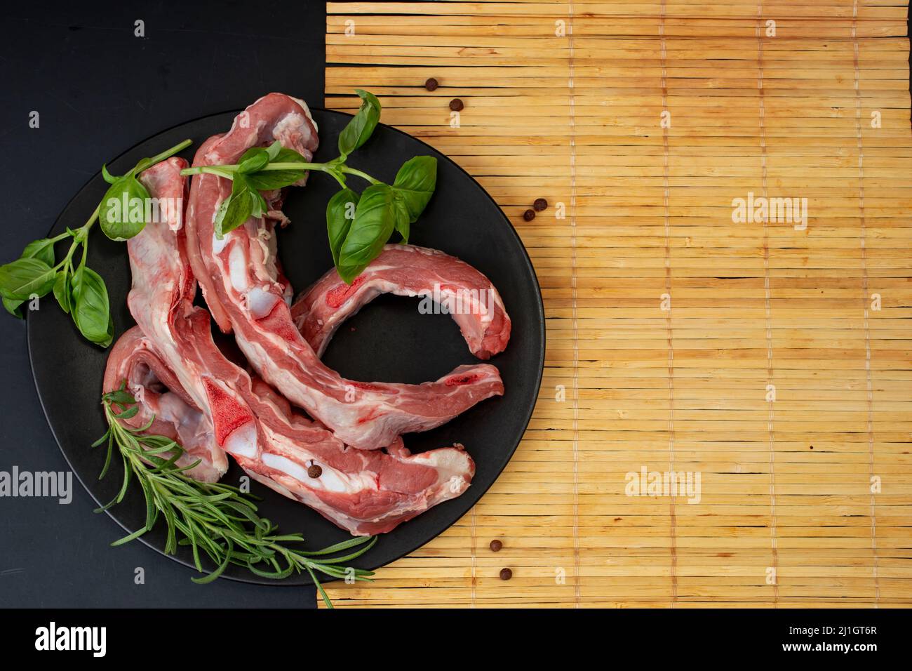 Rinderrippen mit Rosmarin und Basilikum auf einer schwarzen Keramikplatte, Bambusmatte und leerer Platz für ein Rezept Stockfoto