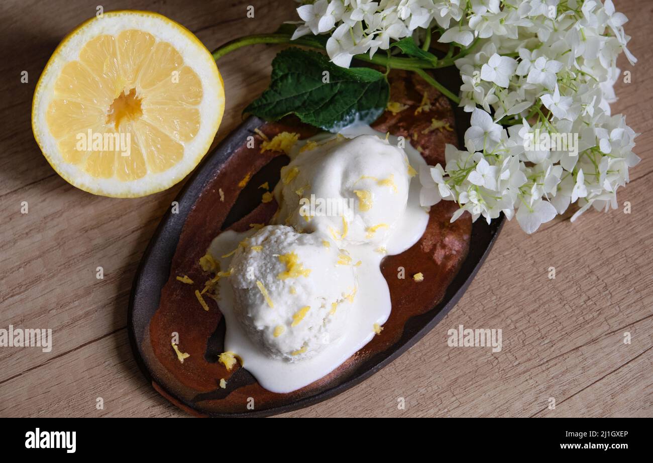 Hausgemachtes Bio-Eis auf dem Tisch in einer handgefertigten Keramikplatte mit einer halben Zitrone und einem Zweig aus weißem Flieder. Stockfoto