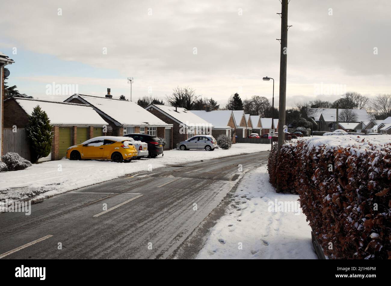 Bungalows entlang einer schneebedeckten Straße durch ein vorstädtisches Wohngebiet in Großbritannien im Winter Stockfoto