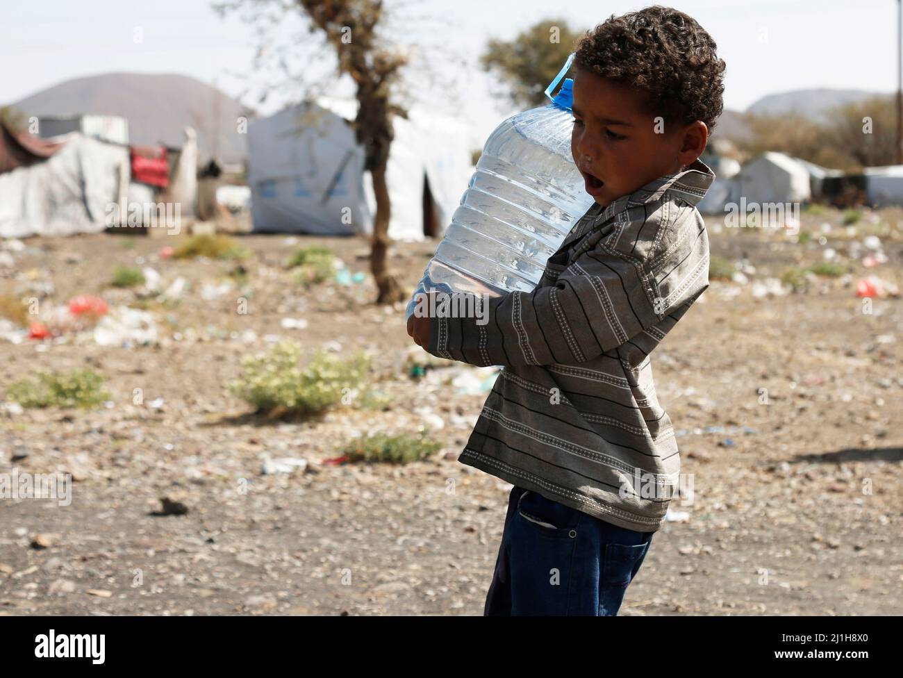 Sanaa, Jemen. 25. März 2022. Ein Kind trägt am 25. März 2022 im Lager für Binnenvertriebene in Dharawan in der Nähe von Sanaa, Jemen, eine Flasche Wasser mit sich. Der Jemen befindet sich seit Ende 2014 in einem Bürgerkrieg, als die vom Iran unterstützten Huthi-Milizen die Kontrolle über mehrere nördliche Provinzen übernommen und die von Saudi-Arabien unterstützte jemenitische Regierung von Präsident Abd-Rabbu Mansour Hadi aus der Hauptstadt Sanaa vertrieben haben. Quelle: Mohammed Mohammed/Xinhua/Alamy Live News Stockfoto