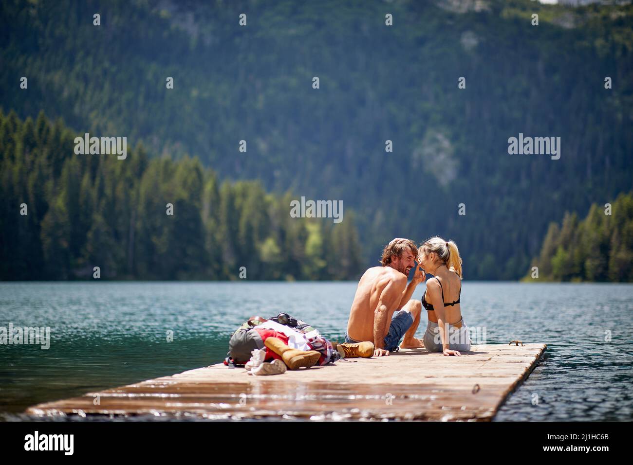 Schönes verliebtes Paar, das auf einem hölzernen Steg am See sitzt. Liebe, Abenteuer, Zweisamkeit, Naturkonzept Stockfoto