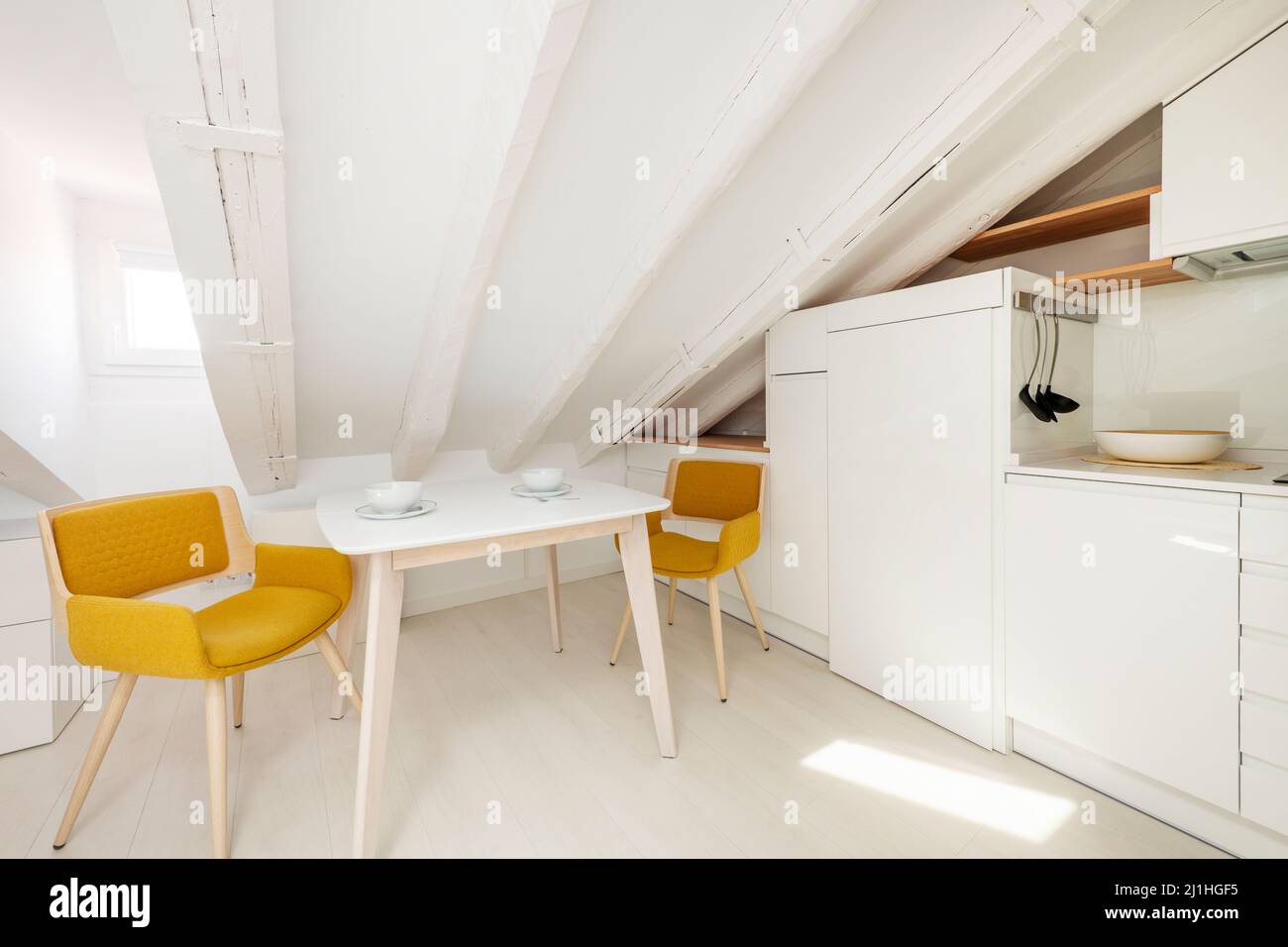 Esstisch neben weißer Küche mit Holzregalen in Dachgeschoss-Wohnung Stockfoto