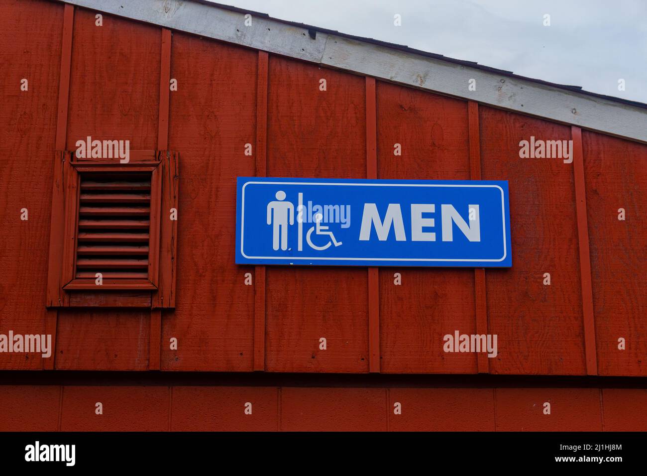 Badschild für Männer auf der Oberseite eines Gebäudes neben dem Dach, blau und weiß vor einer roten Wand. Stockfoto