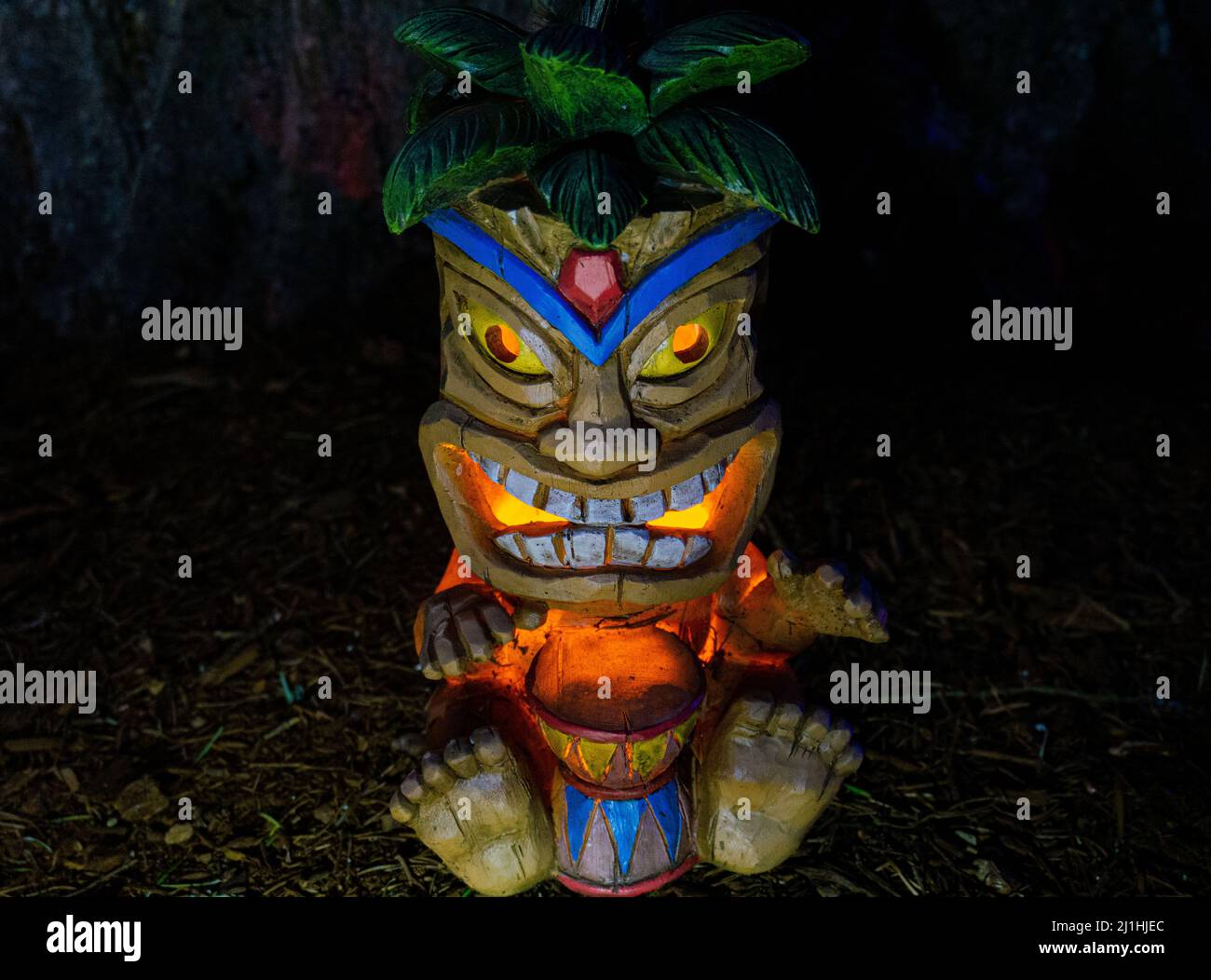 Nachts Tiki Statue mit Rinde von Baumstamm im Hintergrund. Stockfoto