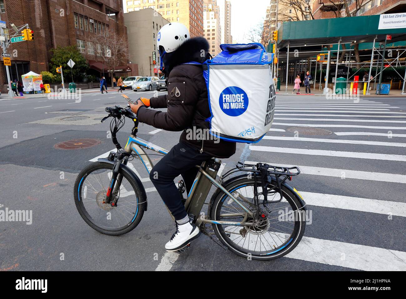 Eine Person, die keine Lieferung mehr für einen Kühlschrank auf einem E-Bike hat, hält ein Smartphone mit Kartenanweisungen, während sie an einer Kreuzung in New York City pausiert, 3. März 2022. Stockfoto