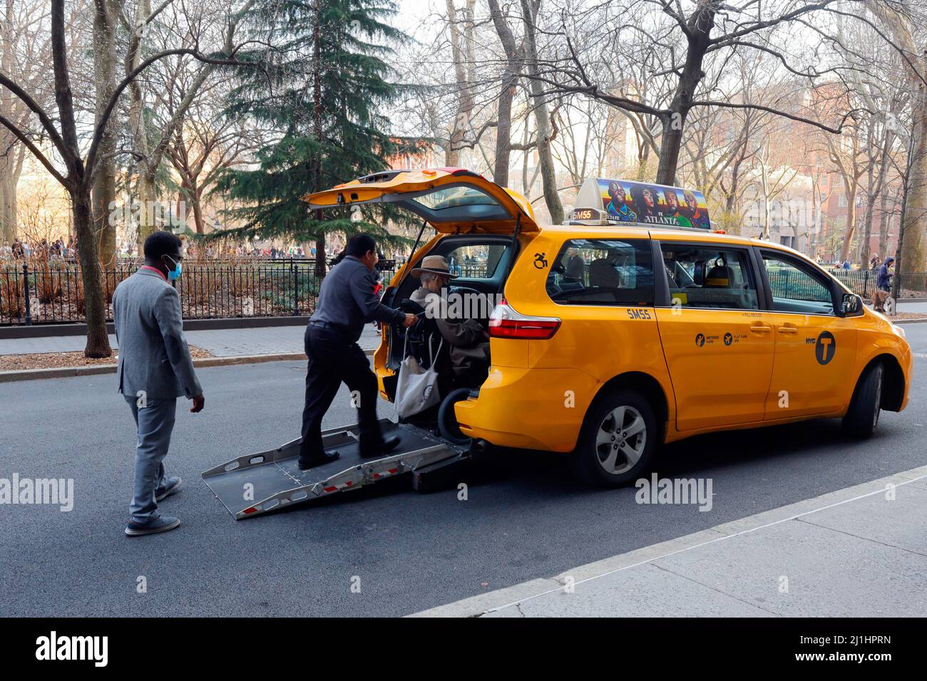 Ein Taxifahrer aus New York hilft einem Rollstuhlfahrer in ein gelbes Taxi mit einem New York City Taxi mit einer rollstuhlgerechten Rampe hinten. Stockfoto