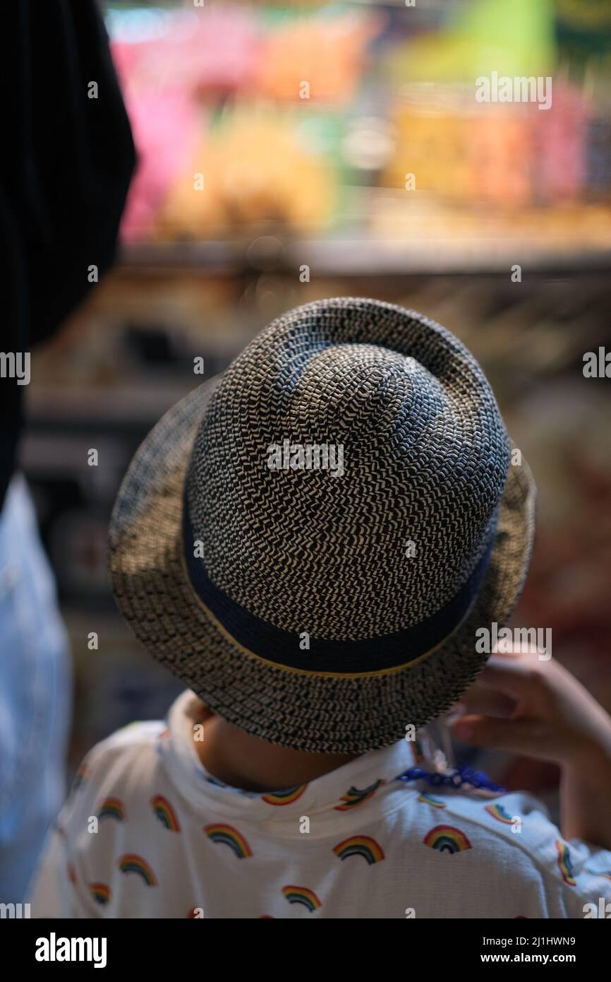 Ein kleiner Junge mit ausgefallener Mütze begutachten eine bunte Vitrine auf dem Nachtmarkt Stockfoto