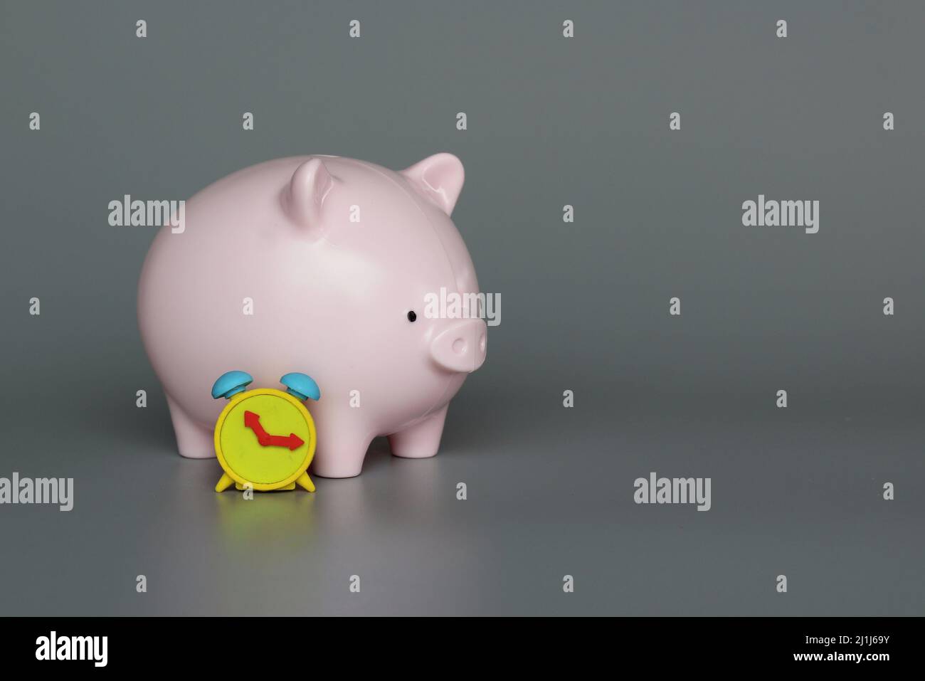 Sparschwein und Wecker auf grauem Hintergrund mit Kopierplatz. Investieren, Inflation, Sparkonzept. Stockfoto