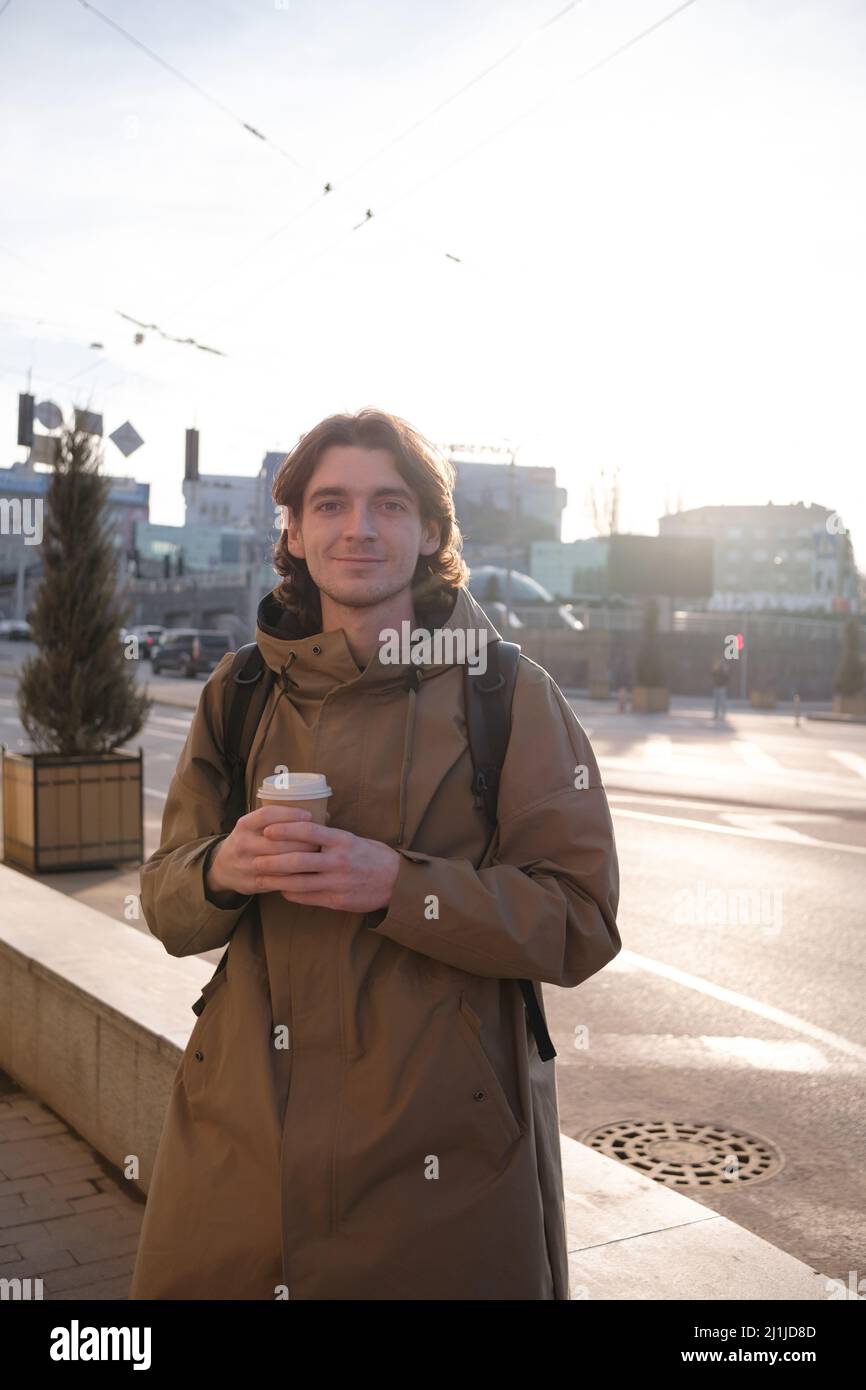 Glücklicher lächelnder Geschäftsmann, der mit einer Kaffeetasse und einem modernen Smartphone im Freien zur Arbeit geht, erfolgreicher Arbeitgeber, der in der Pause Mobiltelefon verwendet Stockfoto