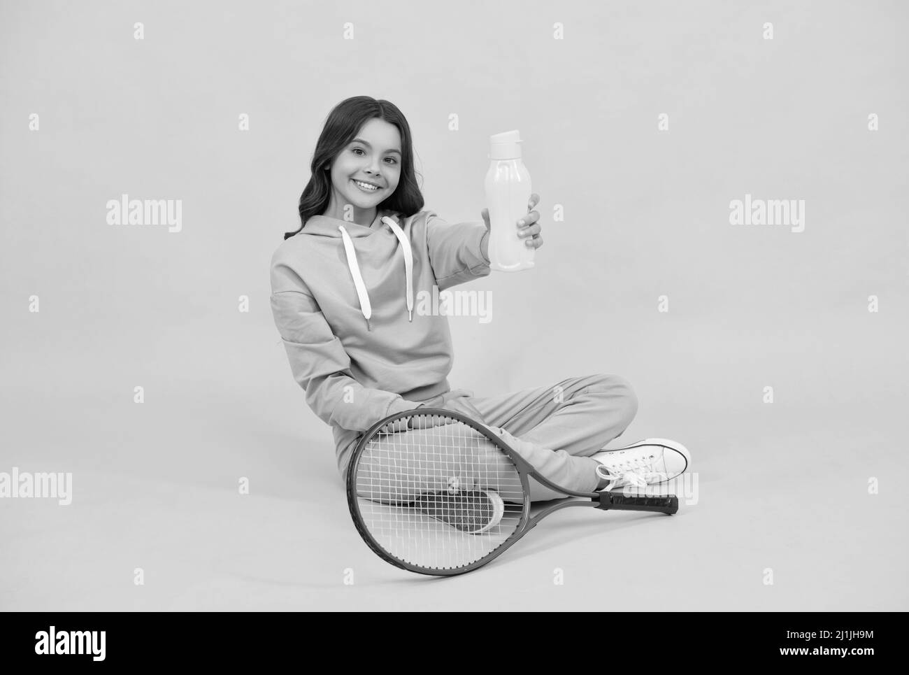 Kind mit Tennisschläger. Jugendliches Mädchen trinken Wasser nach dem Sporttraining. Badmintonspieler entspannen. Stockfoto