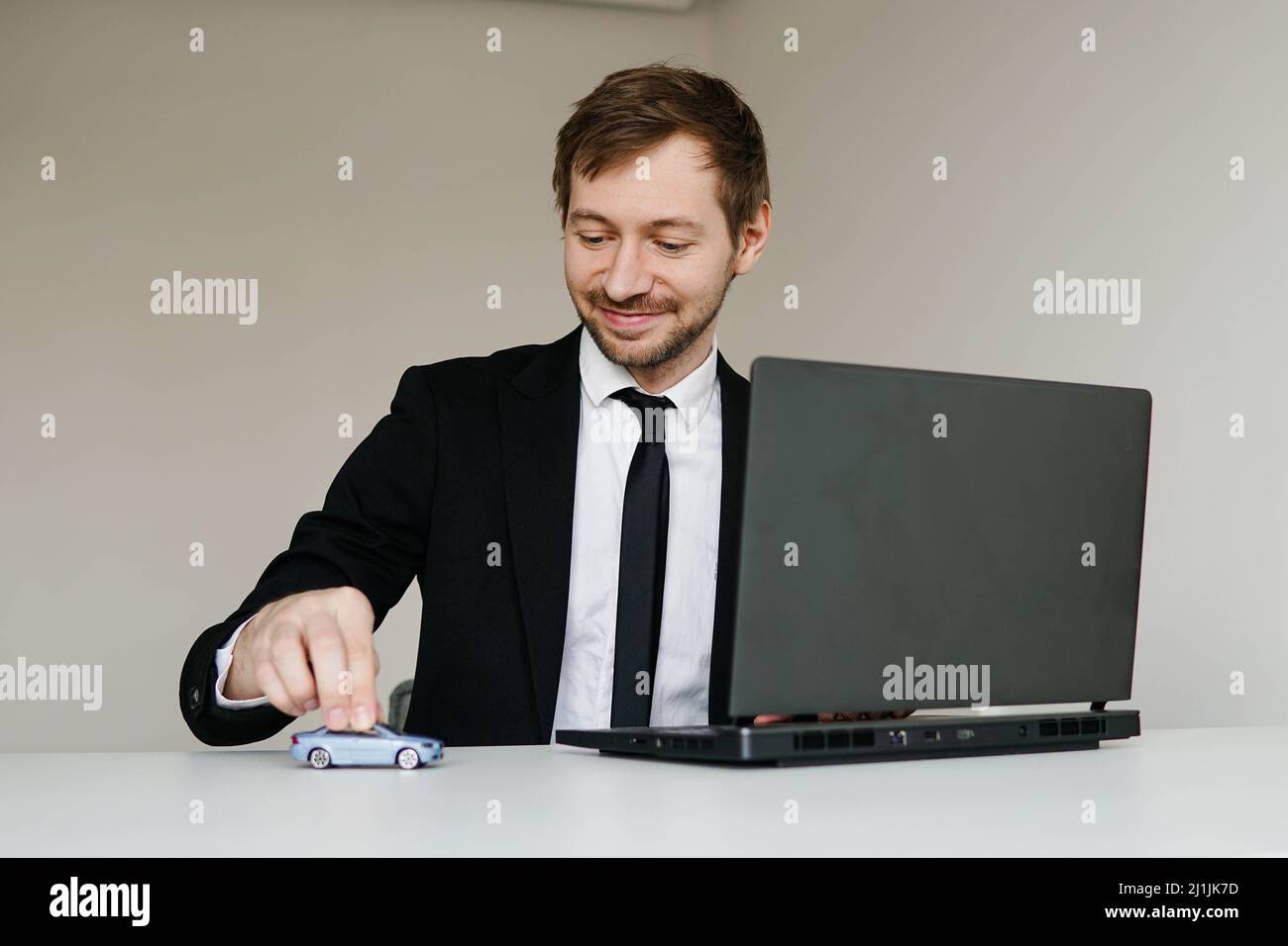 Junger Geschäftsmann im Anzug, der mit einem kleinen Auto auf dem Tisch in seinem Büro spielt Stockfoto