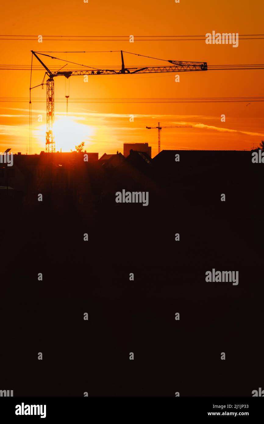 Hohe Baukran Silhouette in orange Himmel Sonnenuntergang zeigt Baustelle mit Engineering für moderne Gebäude und Stadtentwicklung Architekten Stockfoto