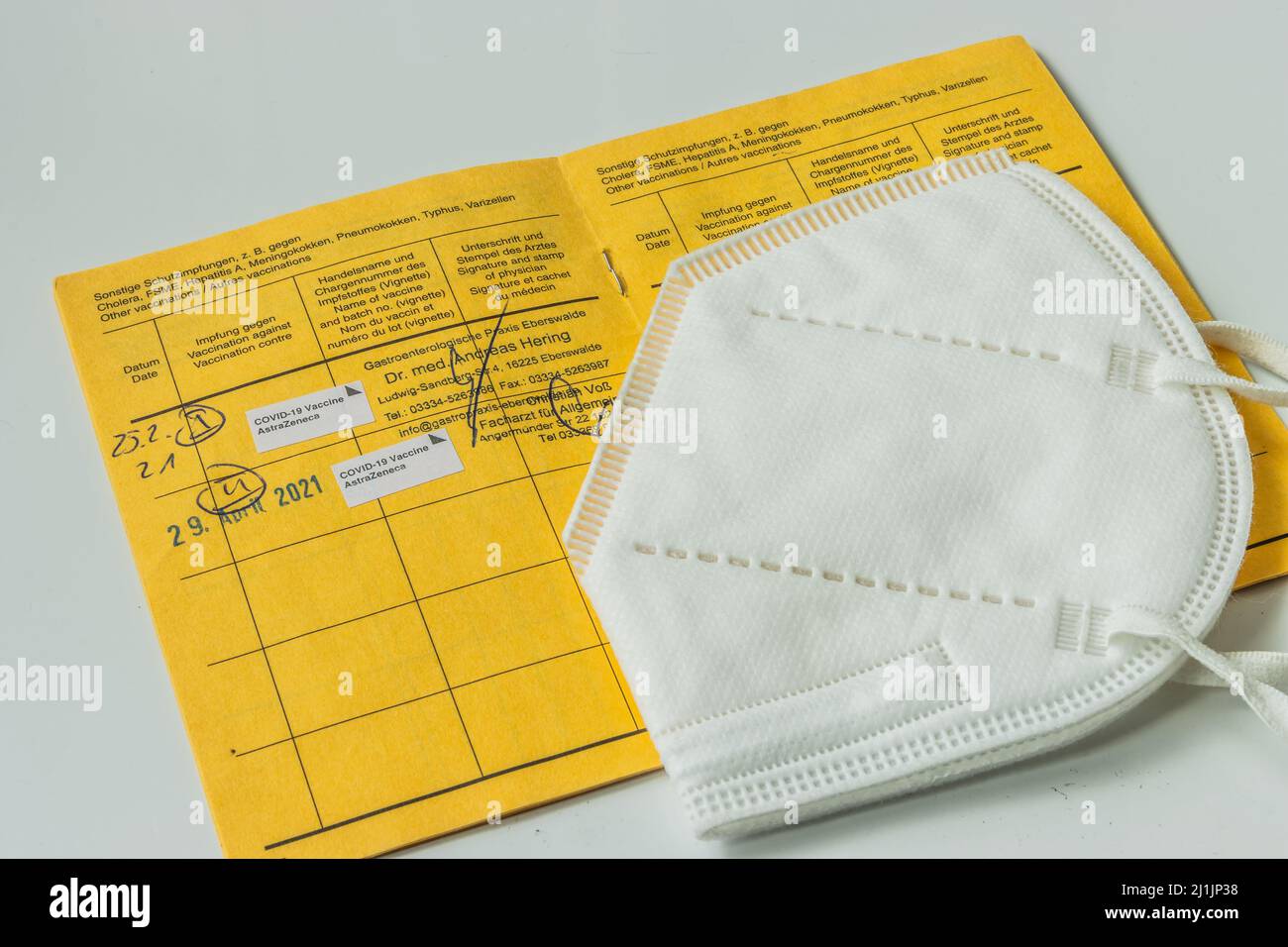 Offene internationale Impfkarte mit weißer Gesichtsmaske. Eintritt von zwei Impfungen gegen das Coronavirus. Seite von der gelben Impfung Stockfoto