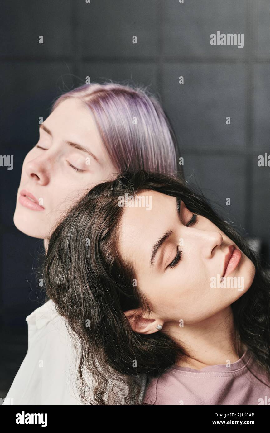 Heitere junge kaukasische Lesben mit geschlossenen Augen, die sich gegen eine gestapelte Wand zurücklehnen Stockfoto