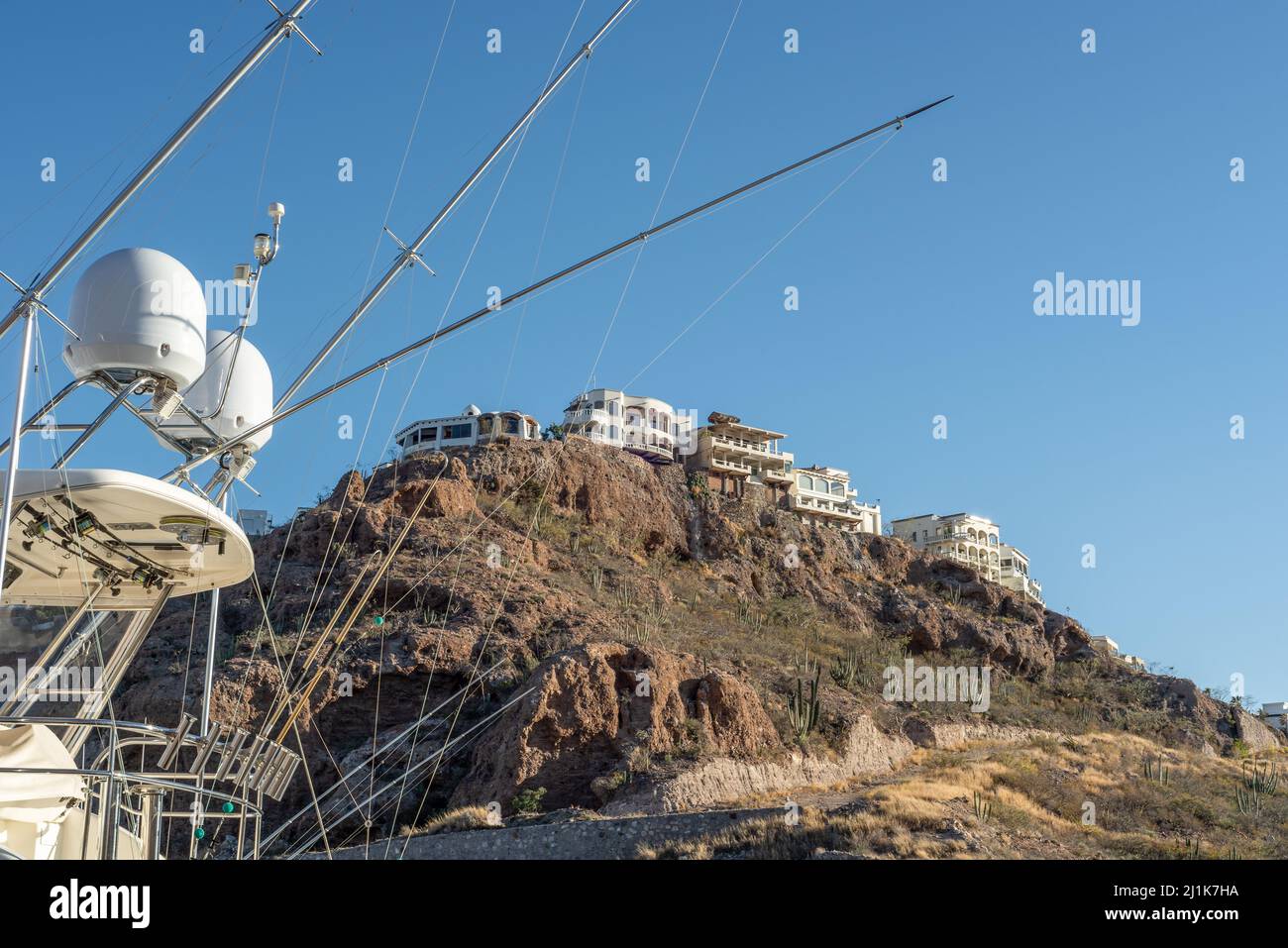 Schießen über das Heck eines Fischerbootes mit Satellitenkuppeln, Auslegerstangen mit Angelschnur, zu Häusern auf einem felsigen Hügel, San Carlos, Sonora, MX. Stockfoto