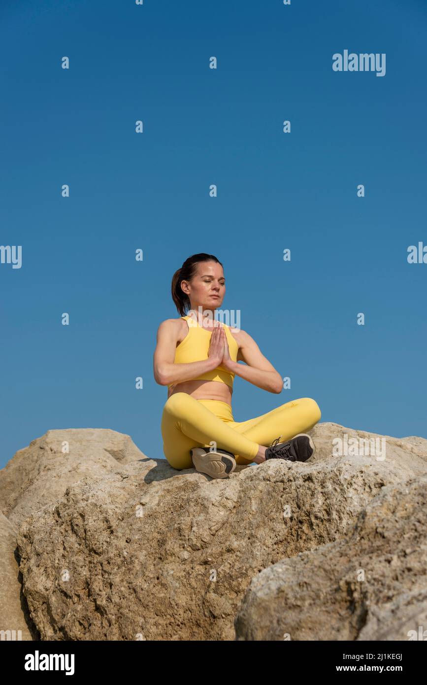 Frau, die Yoga-Meditation macht, sitzt auf Felsen. Gesunder Körper und Geist. Stockfoto
