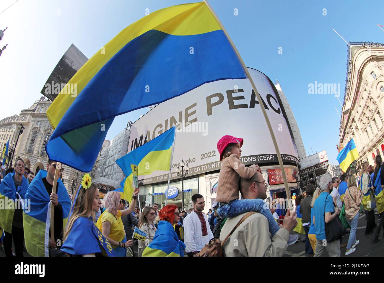 London, Großbritannien. 26. März 2022. Teilnehmer an den Londoner Ständen mit der Ukraine marschieren in London am Piccadilly Circus vorbei, wo Yoko Onos Imagine Peace zur Unterstützung der Ukraine gegen die russische Invasion und den Krieg gezeigt wurde.Quelle: Paul Brown/Alamy Live News Stockfoto