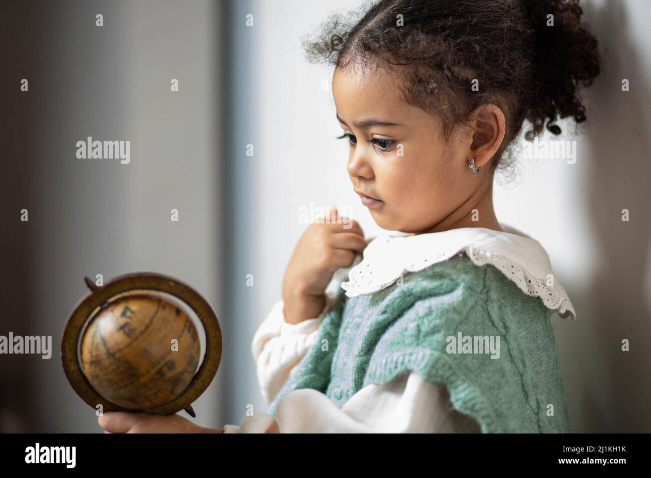 Kleines multiethnisches Mädchen, das in ihren Händen auf hölzernen Globus schaut Stockfoto