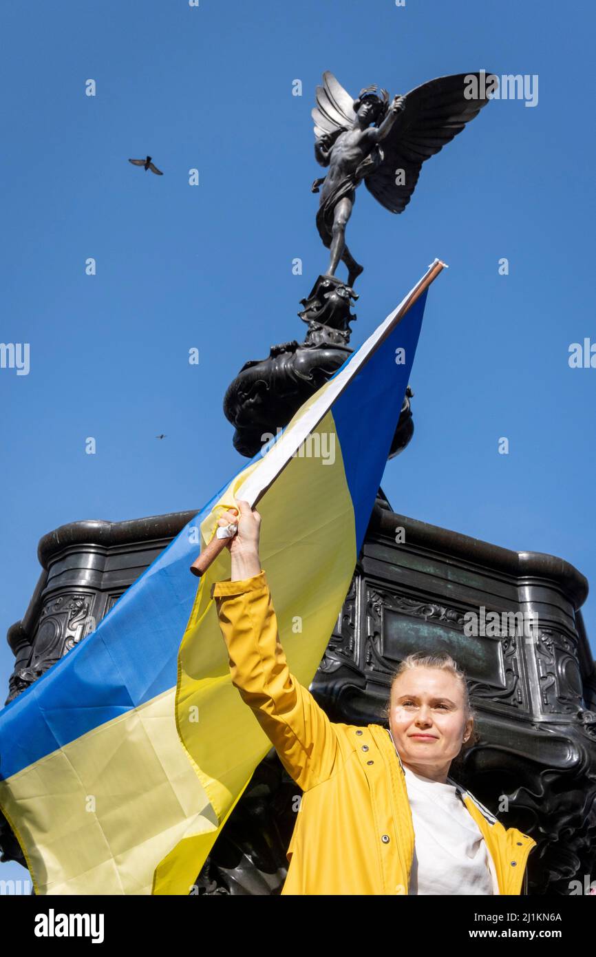 Eine ukrainische Frau hält ihre Nationalflagge unter der Statue des Eros im Piccadilly Circus während des Anti-Kriegs-protestmarsches durch das Zentrum Londons gegen die russische Invasion in der Ukraine am 26.. März 2022 in London, England. Der durchmarsch wurde vom Londoner Bürgermeister Sadiq Khan organisiert. Stockfoto