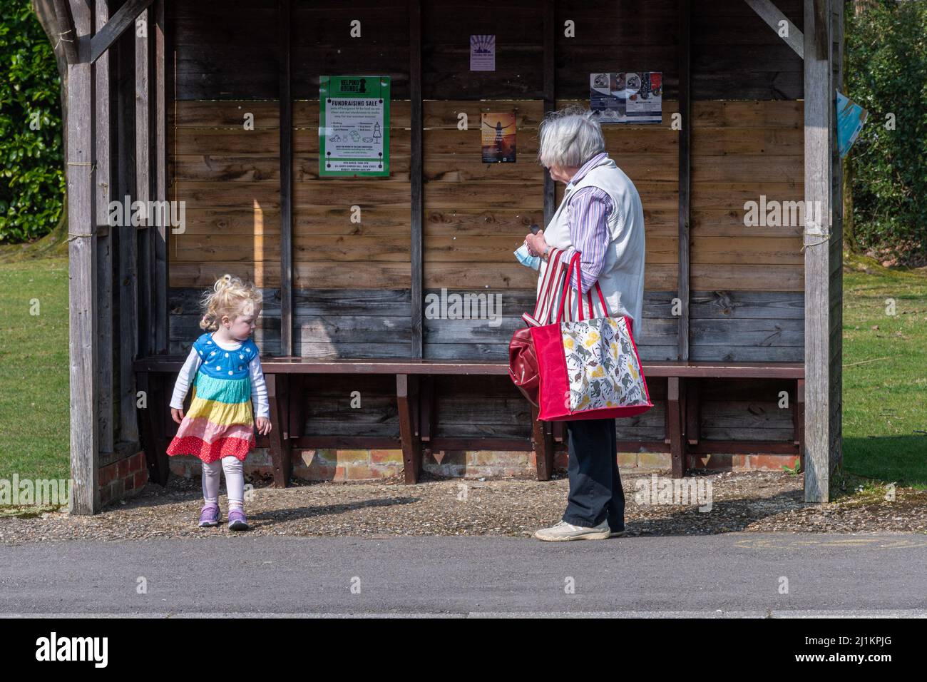 Großmutter, die sich um ihre junge Enkelin gefreut hat, die an einer Bushaltestelle in England, Großbritannien, wartet Stockfoto
