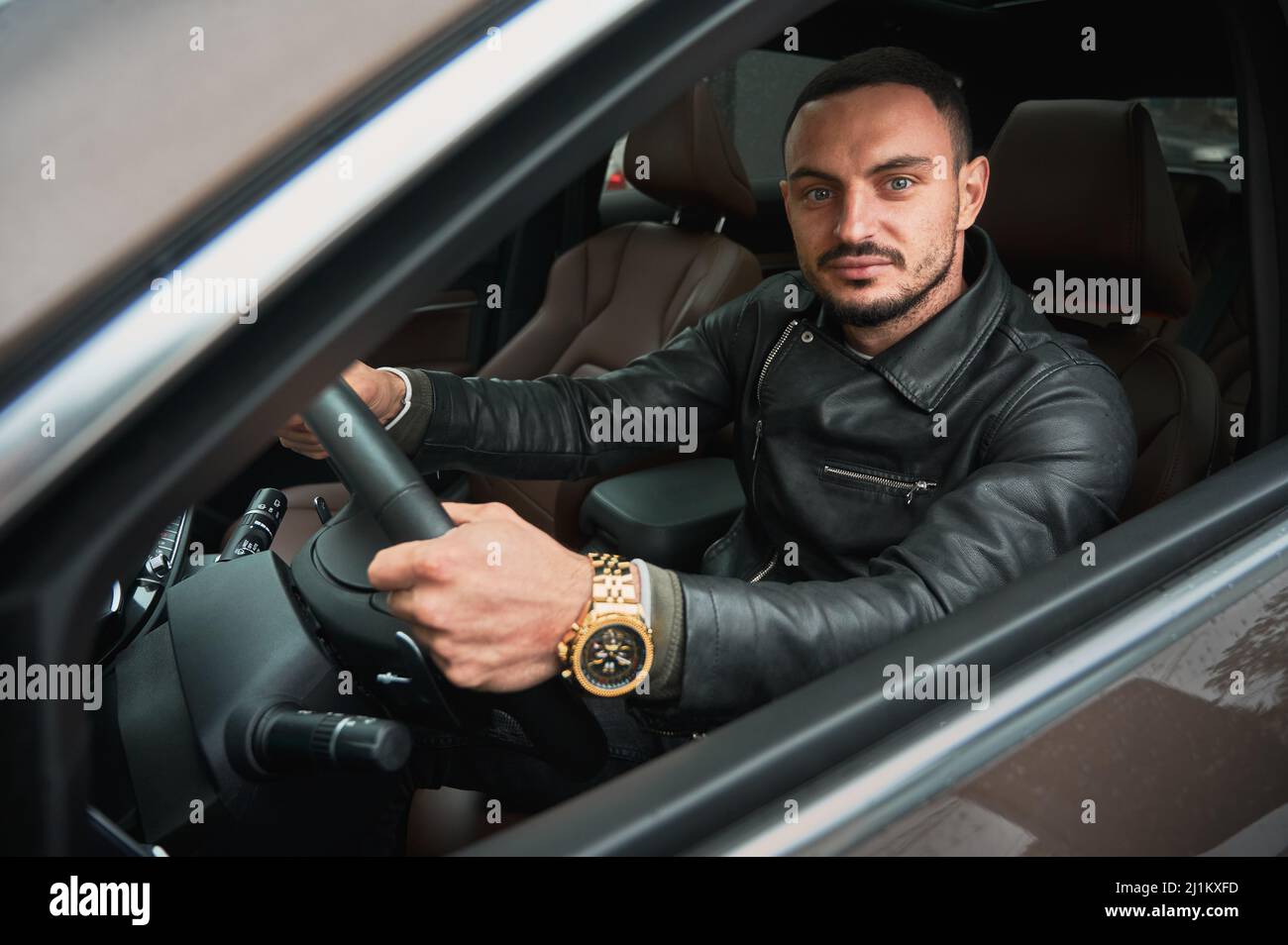 Porträt eines hübschen jungen Mannes, der ein modernes Auto fährt. Typ in legerer Kleidung und goldener Uhr. Stockfoto