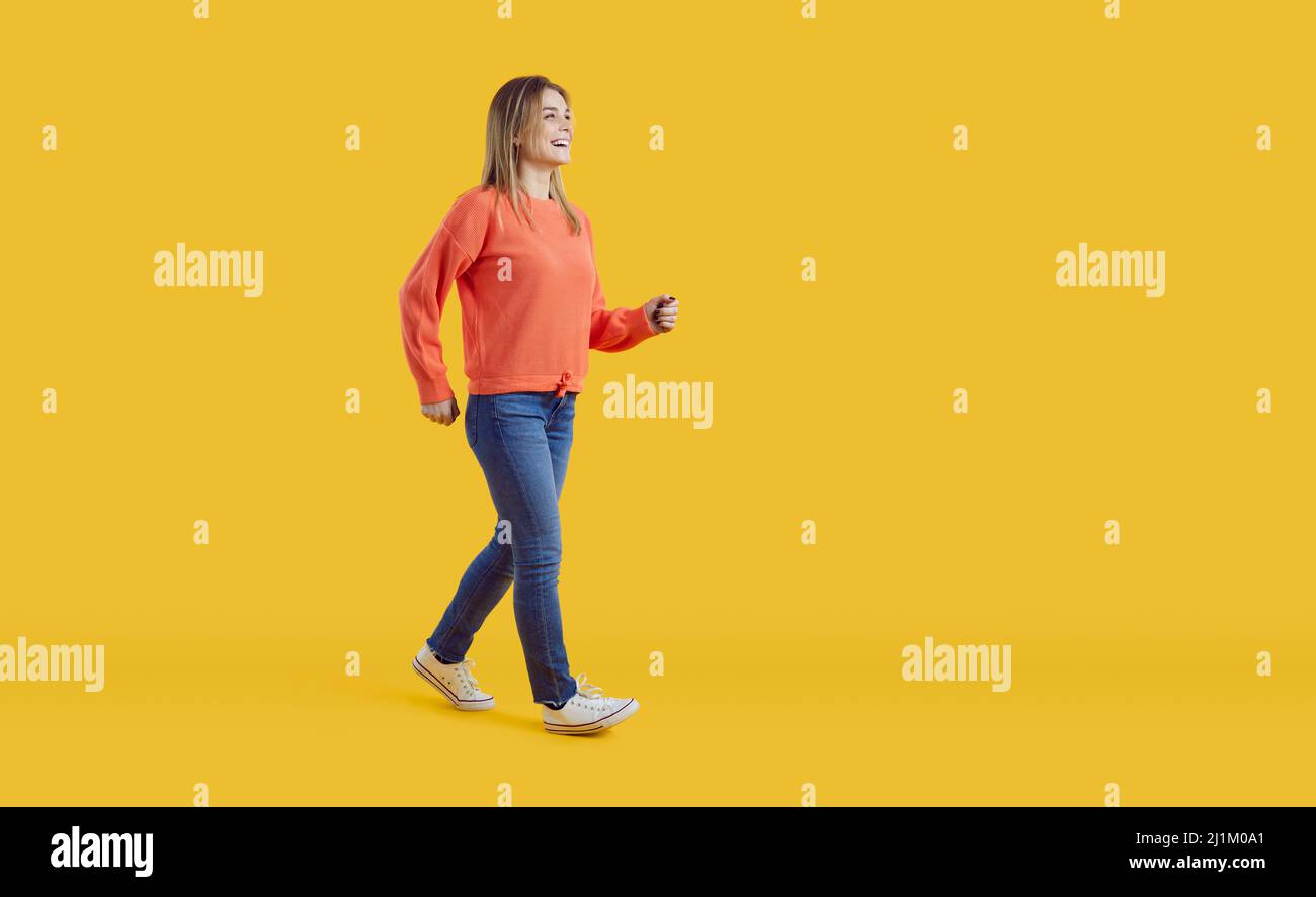 Ganzkörperaufnahme einer glücklichen Frau, die vor einem gelben Studiohintergrund vorwärts läuft Stockfoto