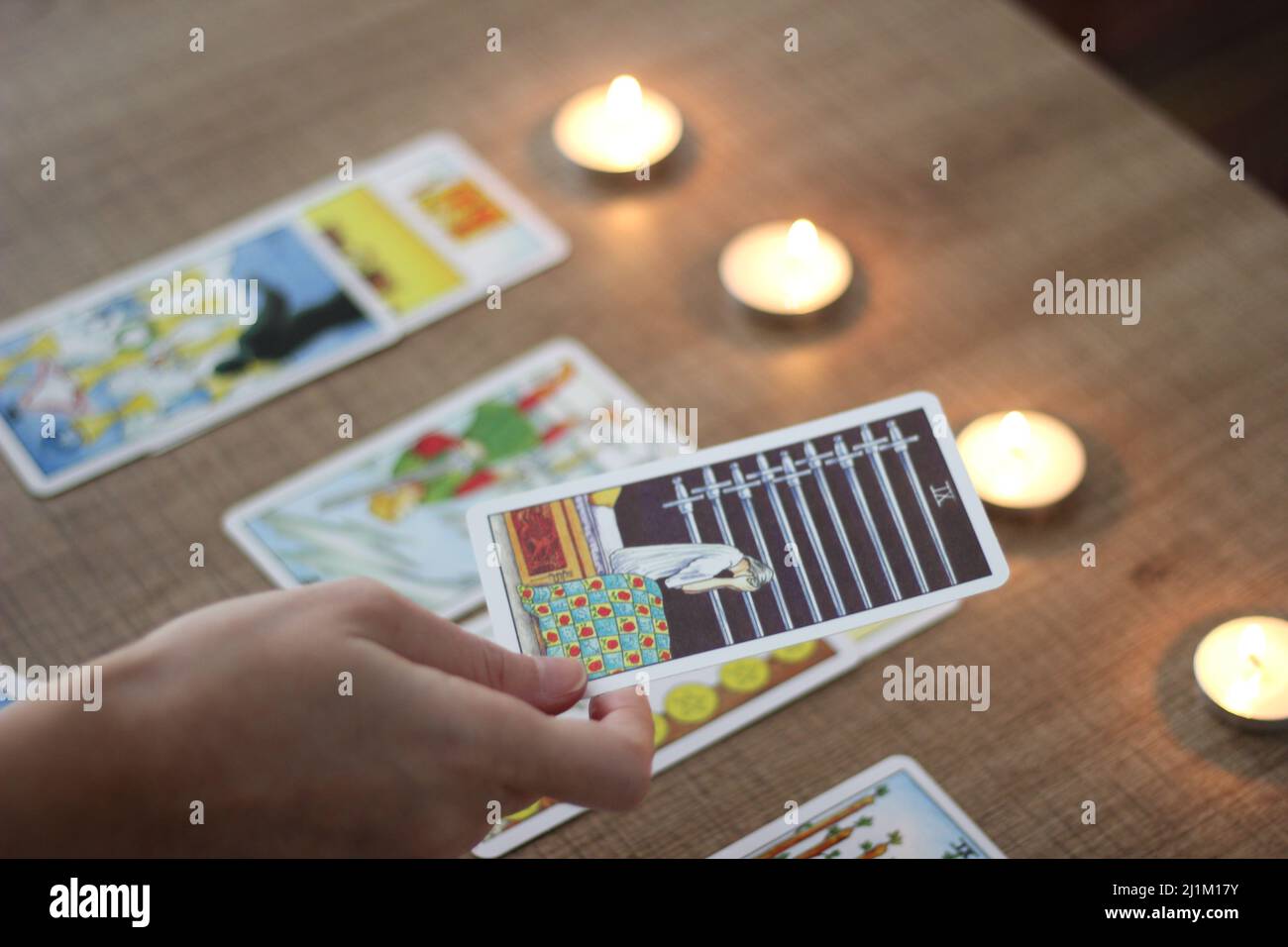 Istanbul, Türkei, 06 2022. März: Wahrsagerin, zeigt oder hält ausgerichtete Tarot-Karten, die mit der Hand auf einem braunen Holztisch gelesen werden, brennende Teekerzen. Stockfoto