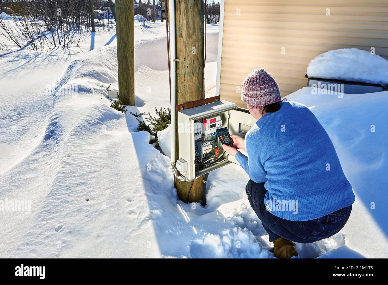 Outdoor-Elektrotafel mit einem elektrischen Zähler auf dem Land im Winter nimmt Frau Messwerte ab und berechnet den Stromverbrauch mit Stockfoto