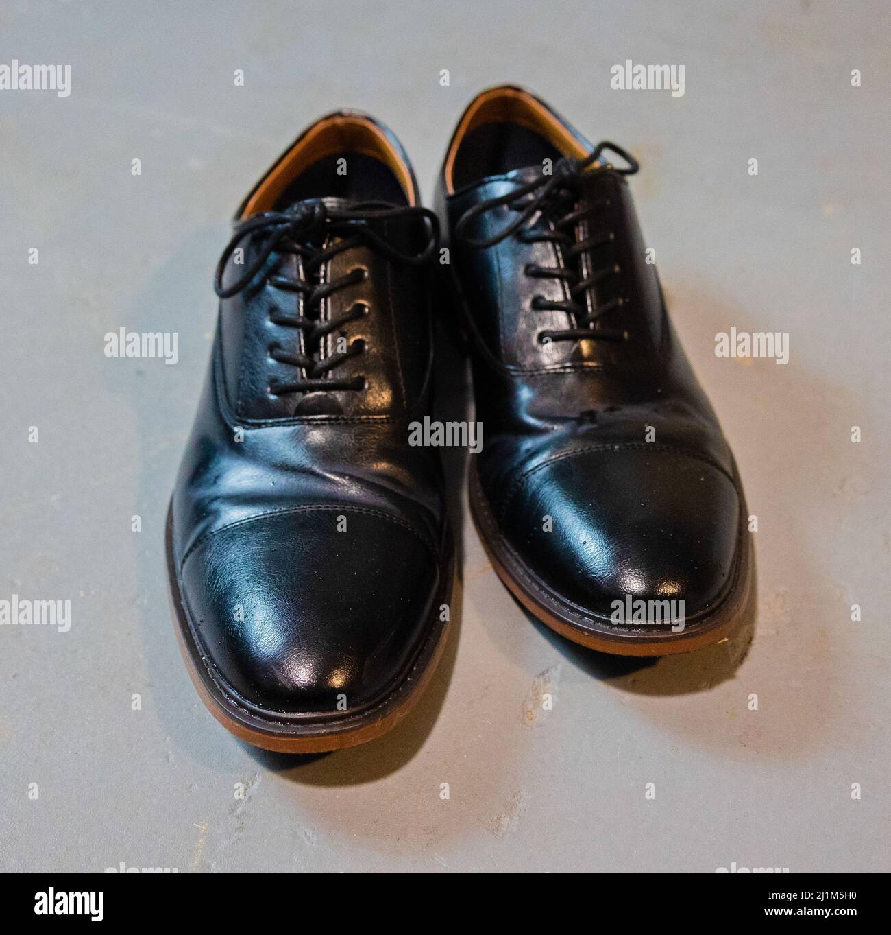 Schuhe mit schwarzen Kleidern und braunen Rändern auf grauem Zementboden. Alles gefesselt. Stockfoto