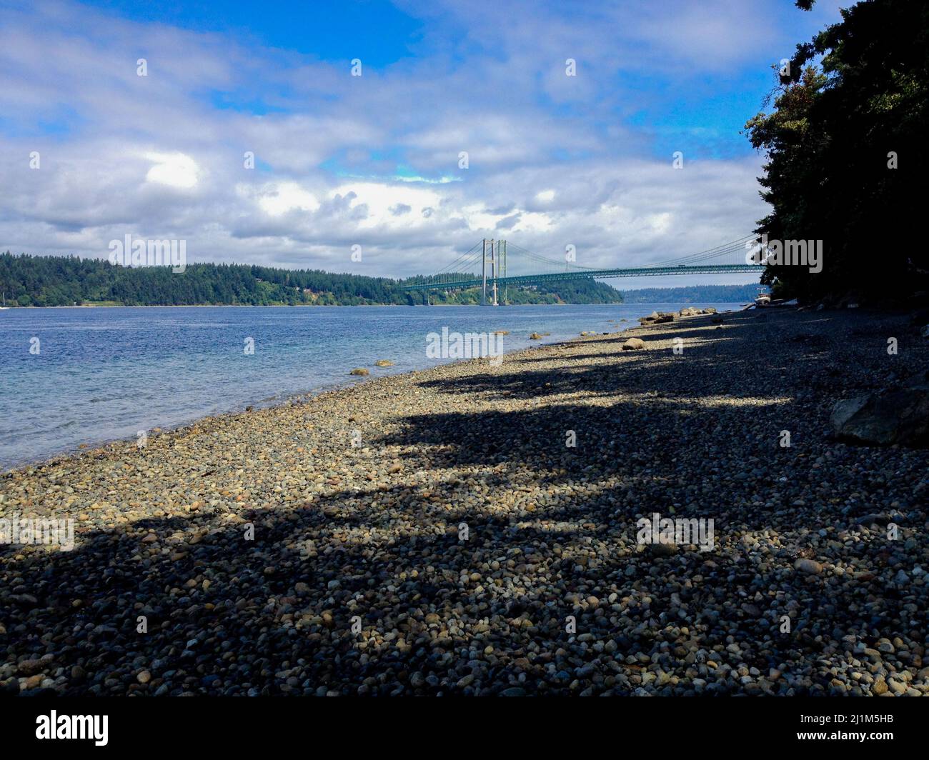 Felsiger Strand mit wunderschöner Brücke in der Ferne, die sich über massive Wassermassen erstreckt. Stockfoto