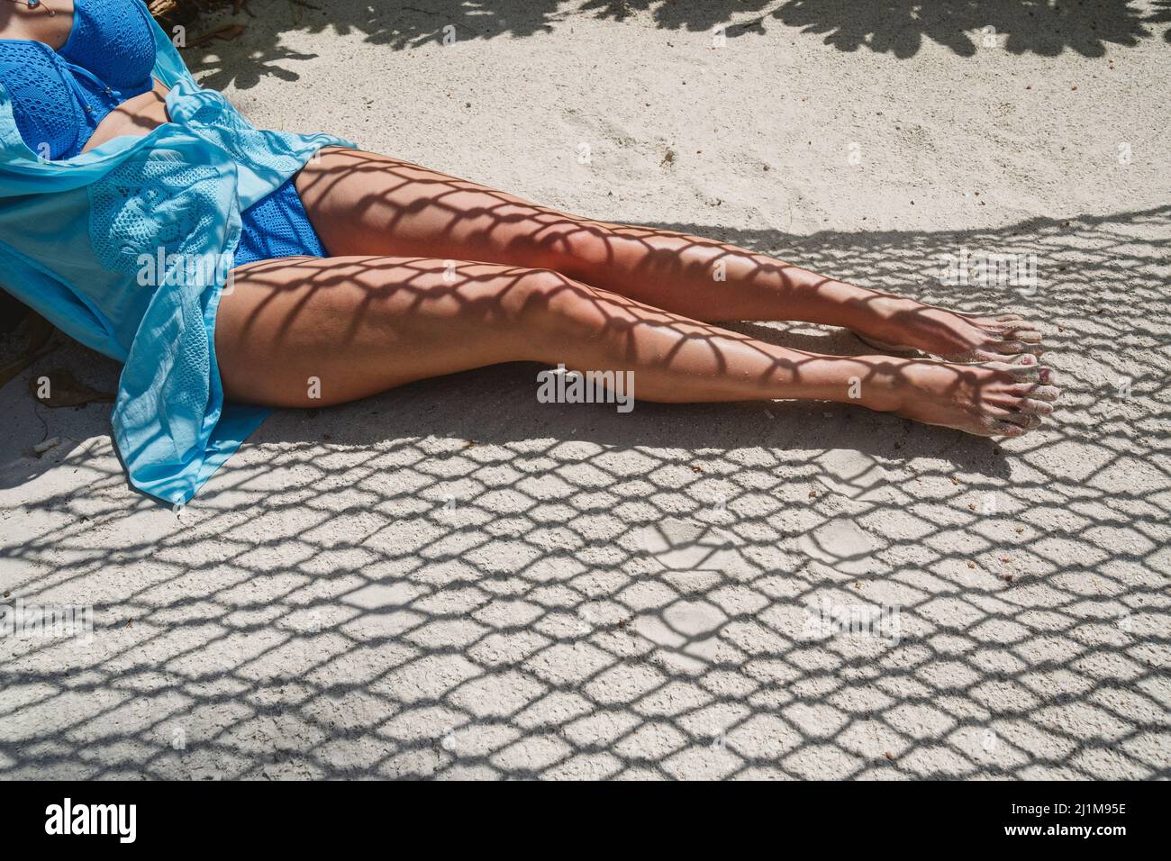 Frauenfüße auf dem Sand mit dem Schatten einer Hängematte. Stockfoto