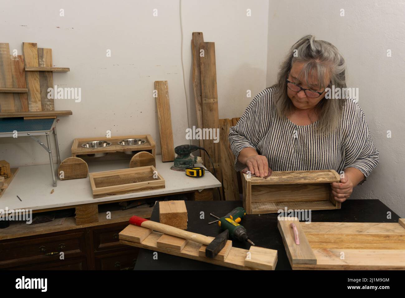 Weißhaarige Frau bei der Arbeit in ihrer Werkstatt aus recyceltem Holz Stockfoto