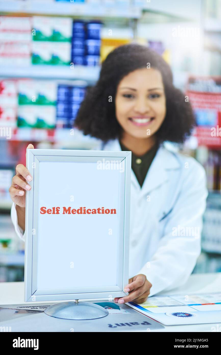 Haben Sie unseren Selbsthilfeservice ausprobiert? Aufnahme einer jungen Frau, die am Schalter einer Apotheke ein Schild mit Selbstmedikation zeigt. Stockfoto