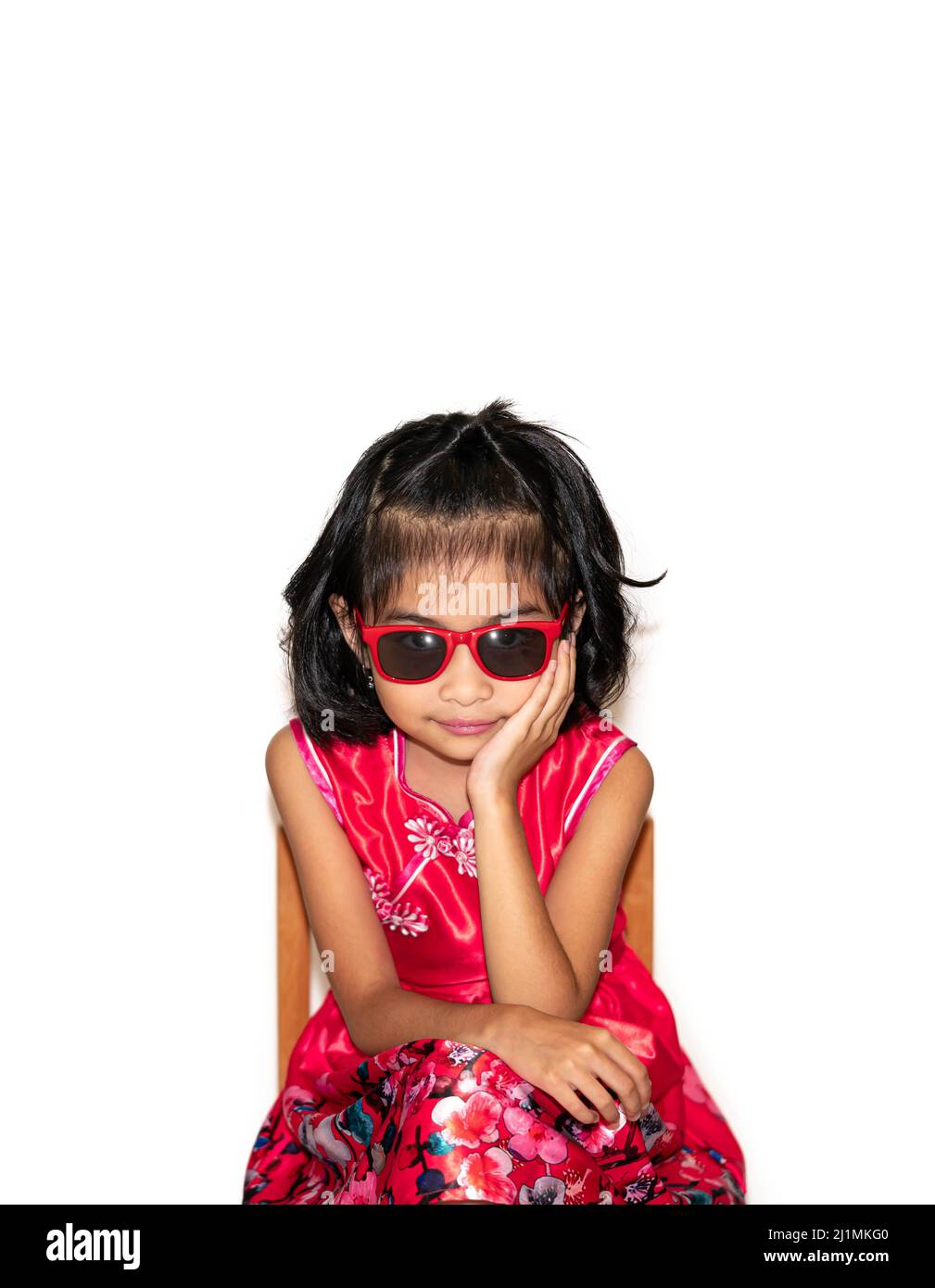 Bild von schönen liitle Mädchen in rotem Kleid trägt Sonnenbrille auf Stuhl sitzen Stockfoto