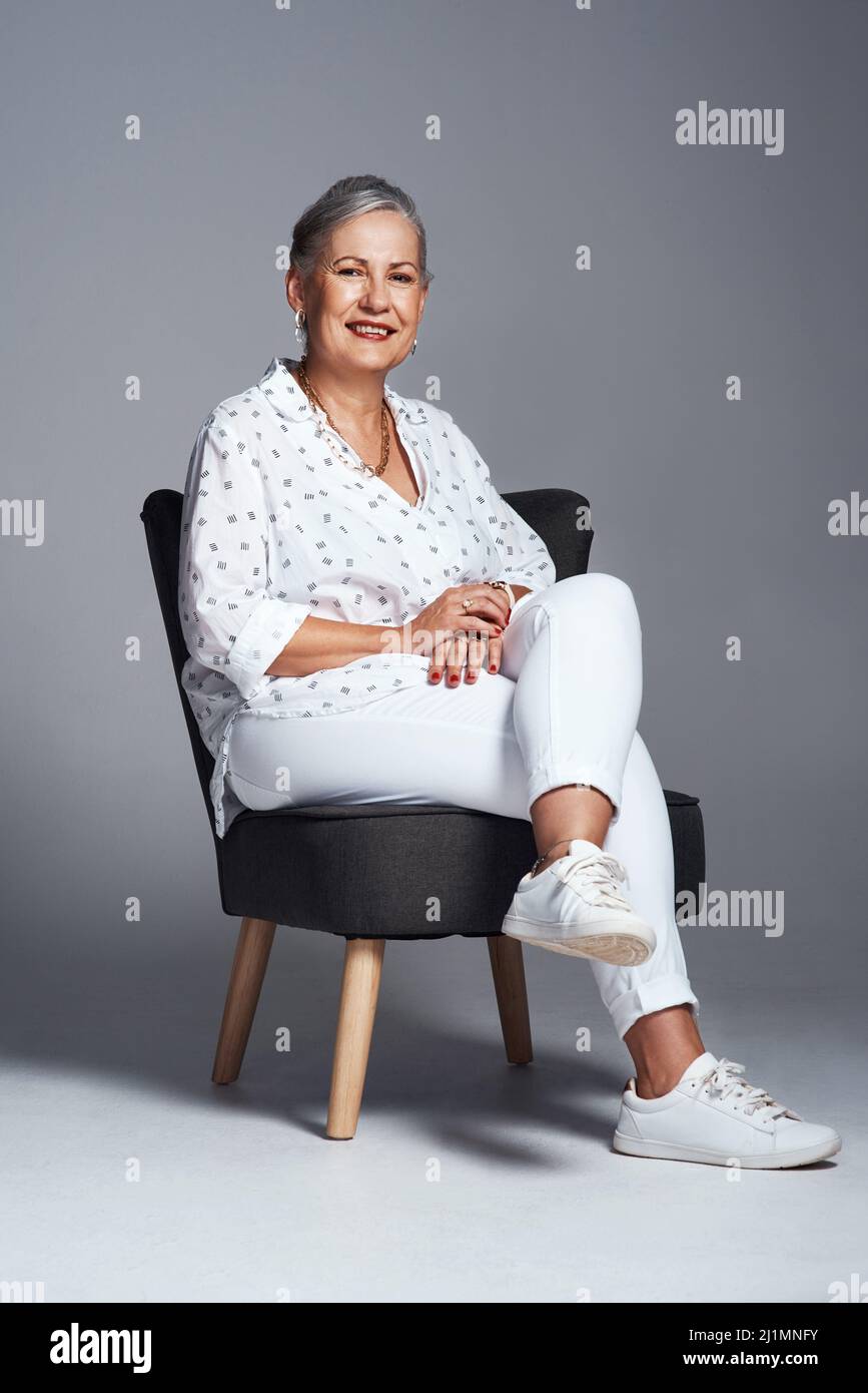 Du bist eine Frau und du bist würdig. Studioaufnahme einer älteren Frau, die auf einem Stuhl vor grauem Hintergrund sitzt. Stockfoto