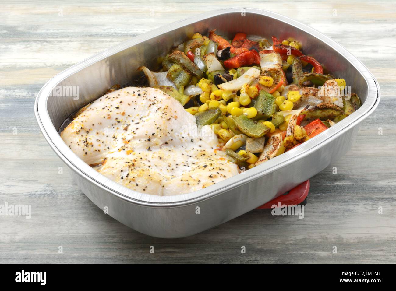 Heiße zwei gebackene Hühnerbrüste mit Mais, Paprika, Bohnen und Zwiebelgemüse in einer Pfanne auf dem Untersetzer Stockfoto