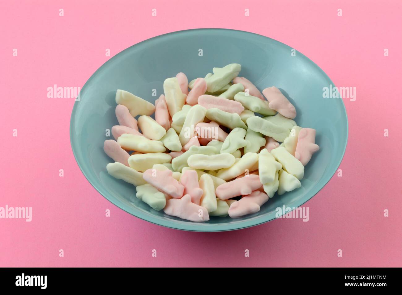 Rosa und weiße Süßigkeitenstücke in blauer Dessertschale auf rosa Hintergrund Stockfoto
