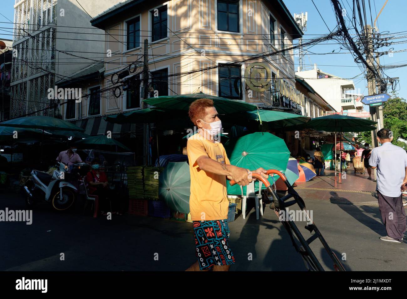 Am frühen Morgen fällt Sonnenlicht auf einen Portier, einen Migranten aus Myanmar, der seinen Wagen auf dem Pak Klong Talat (Markt) in Bangkok, Thailand, schiebt Stockfoto